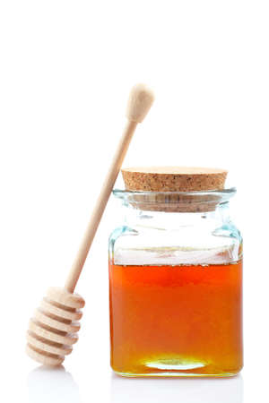 Honey jar and wooden drizzler, reflected on white backgroundの写真素材
