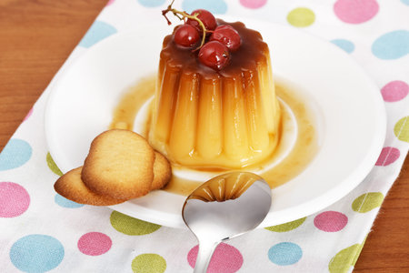 Vanilla cream caramel dessert with red currants and two cookies on white dish