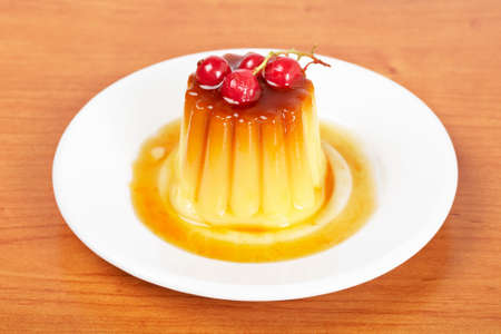 Close-up of a vanilla cream caramel dessert with red currants on white dishの写真素材