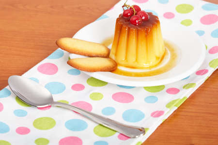 Vanilla cream caramel dessert with red currants and two cookies on white dish. Shallow depth of fieldの写真素材