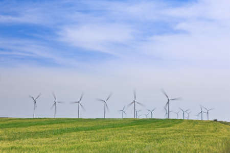 Wind turbines farm in green field over cloudy skyの写真素材