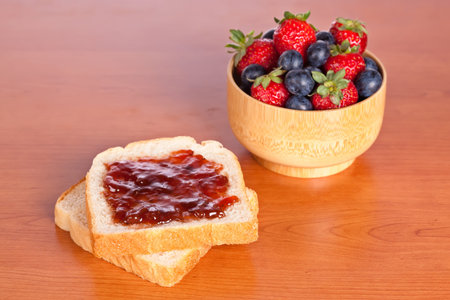 Two toast with jam, blueberries and strawberries in a bowl on wooden background. Shallow depth of...