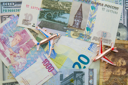 Colorful flat lay of world currencies including Russian, Chinese, USD, euros with 2 model planes on topの写真素材