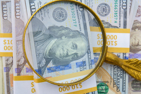 Magnifying glass showing detail of hundred dollar bills on a pile of 10,000 strap bundlesの写真素材