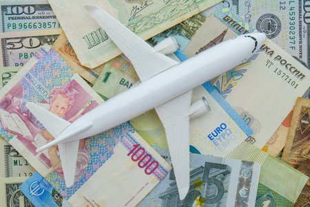 Passenger plane sitting on world currency bills including ruble, euro, USD, showing concept high cost of flying, travelの写真素材