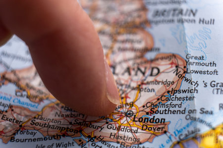 Close up of finger pointing to London, England on detailed colorful map with selective focus,...