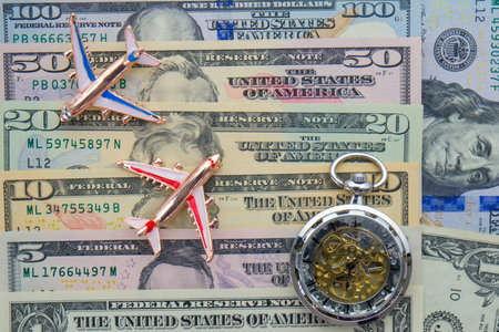 Passenger planes and pocket watch sitting on US currency bills of different denominations showing concept high cost of flying, timeの写真素材