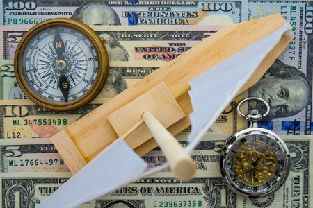 Toy sailboat, compass, and pocket watch sitting on US currency bills of different denominations showing concept high cost of leisure boating, timeの写真素材