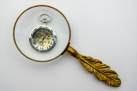 Gold handled magnifying glass viewing a pocket watch with visible gears, isolated on white backgroundの写真素材