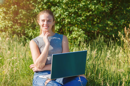 A girl with a laptop in nature among the green grass.の写真素材