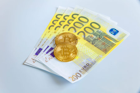 Golden bitcoin coins on the background of 200 Euro paper notes. The concept of trading and the value...