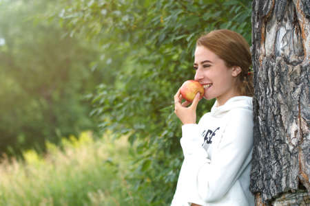 A girl holds a red Apple against a background of green trees. The concept of healthy eating and vegetarianism. There is a copyspaceの写真素材