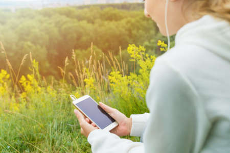 A young woman listens to music with headphones through a smartphone in nature.の写真素材