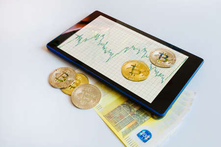Growing chart on the currency exchange on the smartphone screen with bitcoin and paper currency Euro coins.の写真素材