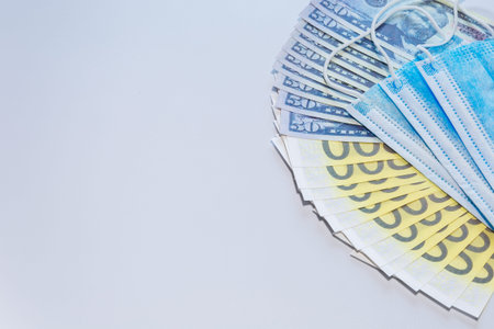 A fan of dollar and Euro bills with medical masks. The concept of drug shortages and their rise in...