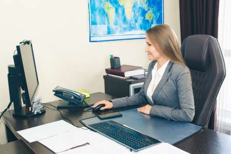 Woman supervisor at the desk in a modern style in a formal suit looks at the computer monitor.の写真素材