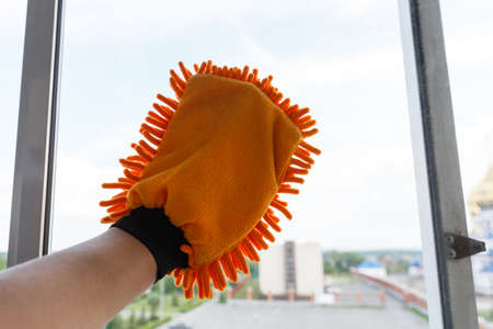 Washing the windows of the glass balcony with a hand mitt. A window-cleaning glove is worn on a mans hand.の写真素材