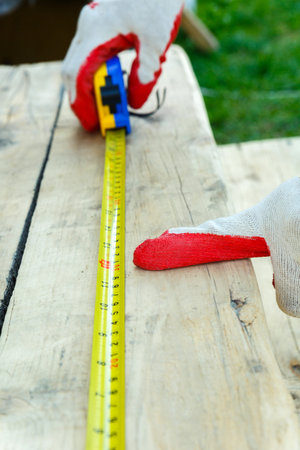 A male hand in work gloves points with the index finger to the length of the measuring tape. Side...