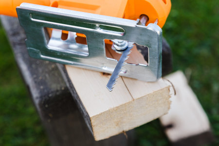 Electric jigsaw and wood board with fresh cut and sawdust.