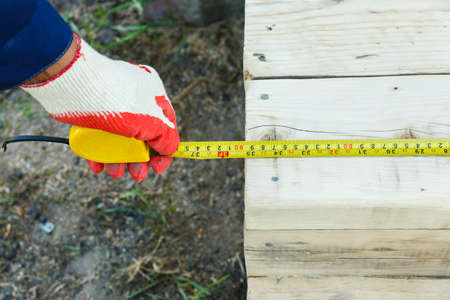 A mans hand holds a measuring tape and measures the length of the board. Measurement of the length of the building material.の写真素材