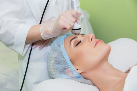 A young woman is lying on the RF-lifting procedure for face skin tightening and face contour...