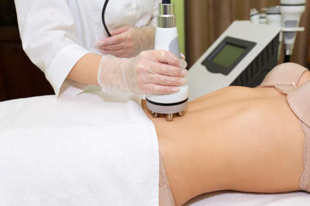 The beautician holds a manipulate to the young woman of the Russian Federation lifting the abdomen. Radiofrequency lifting for body shaping and burning of subcutaneous fat.の写真素材