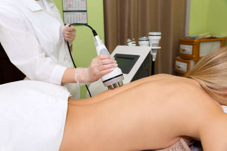 The spa beautician holds the RF-lifting maniple in his hand and runs it along the client's back.の写真素材