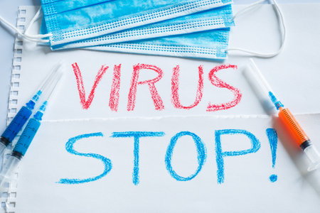 Medical syringes with vaccines of different colors on the background of the inscription stop the virus and medical masks. The concept of a vaccine against viral diseases and protection from bacteria.の写真素材