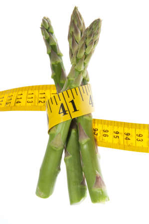 Healthy green fresh raw asparagus wrapped around a yellow tape measure to symbolize a healthy diet, lifestyle or weight loss. Studio isolated on a white background with a clipping path. の写真素材