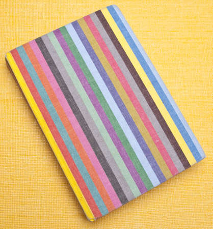 Rainbow striped notebook on a yellow background.の写真素材