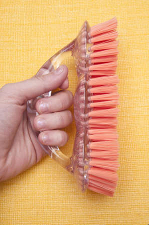 Caucasian hand holds a bright scrub brush on a yellow background in this spring cleaning themed image.の写真素材