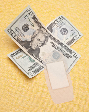 Money with a plaster on a yellow background to demonstrate the cost of health care.