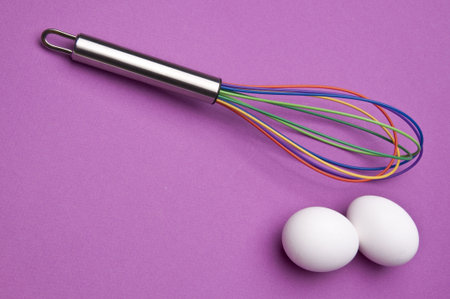 Rainbow Whisk with Eggs on a Vibrant Purple Background.の写真素材