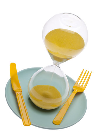 Hourglass on a plate with a fork and knife for food and time conceptual themes.