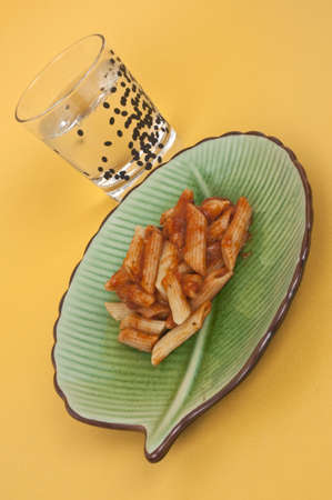 Ziti Dinner on a Green Dish with a Glass of Seltzer Water on a Yellow Background.の写真素材