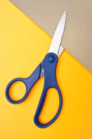 Blue Scissors Cut Brown Paper on a Yellow Background.の写真素材