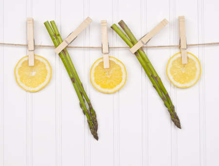Summer Lemon Slices and Asparagus Hanging from a Clothesline on a White Textured Background.の写真素材