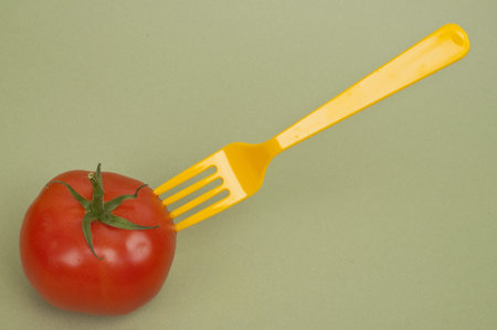 Fresh Tomato with a Yellow Fork on a Green Background.の写真素材