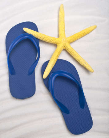 Summer Flip Flop Sandals with a Bright Yellow Starfish on a Sand Background.の写真素材
