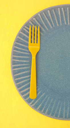 Modern Place Setting with Empty Plate and Plastic Yellow Silverware on Yellow Background.の写真素材