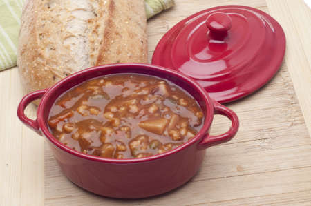 Beef Vegetable Soup in a Crock with Bread in the Background.の写真素材