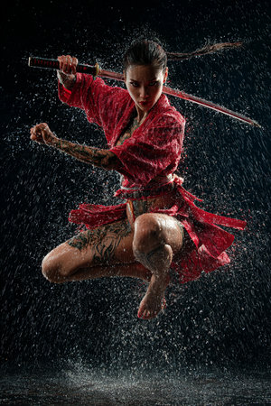 Young woman samurai with katana in water studio on black background.の素材