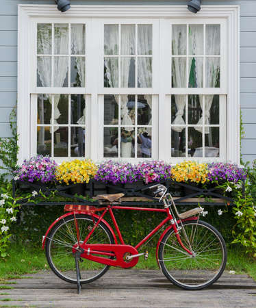 	Red bicycle parked with beautiful flowers adorn the windowsの写真素材