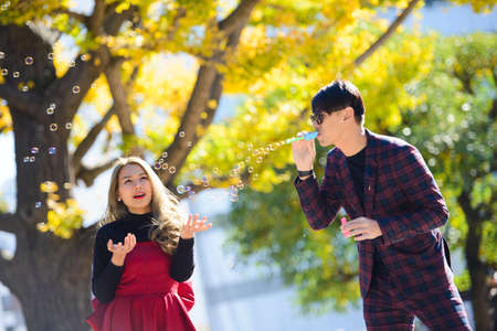 Young asian couple blowing bubbles in autumn sceneの写真素材
