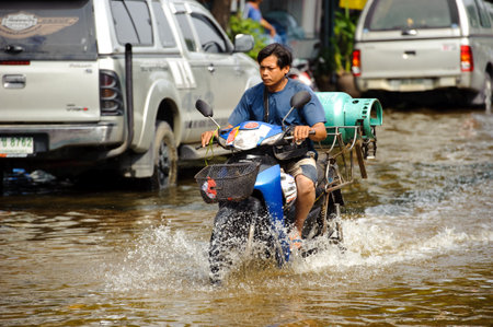 Bangkok, Thailand - November 5, 2011 : A delivery man drives a motorcycle on a flooded street after torrential rain on November 5, 2011 Bangkok, Thailandのeditorial素材