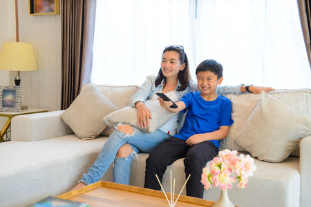 Mother and her son are watching tv while sitting on a couch