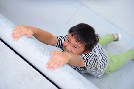 Little boy hanging on wall on hands and trying to climb upの写真素材