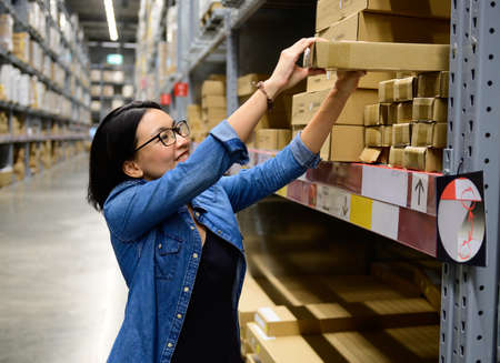 Portrait of woman delivery staff pick up box in warehouseの写真素材