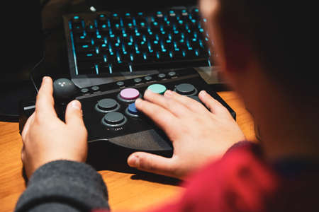 Imperia, Italy, 20/11/2019: Boy who presses the colored button of an arcade pad to play vintage video games, photo of a normal moment of life.の写真素材