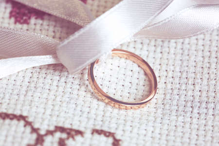 details of a wedding ring with white ribbon and laid on an embroidered fabricの写真素材